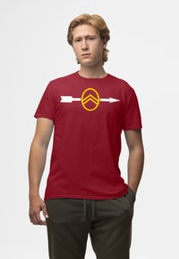Rød bomulds t-shirt med en gul grafik af en cirkel med en chevron og to hvide pile, der fremviser en glat tekstur og standard pasform.