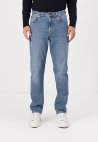 Vaqueros de denim azul claro con un corte recto, diseño de cinco bolsillos y una cinturilla clásica, combinados con zapatillas blancas.