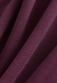 Gros plan d’un tissu tricoté doux et plié de couleur violet foncé montrant une texture fine et un motif côtelé avec des ombres douces.