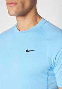 Blå kortermet treningsskjorte med rund hals, med svart Nike-logo på brystet og teksturerte mesh-sider for ventilasjon.