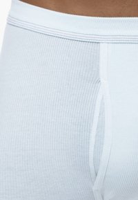 White ribbed underwear with a soft waistband featuring a subtle multicolored stitch. The fabric appears smooth and slightly stretchy.