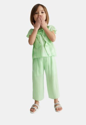 Completo verde chiaro per bambini con un top plissettato e un fiocco, abbinato a pantaloni larghi. Sandali bianchi con cinturini completano il look.