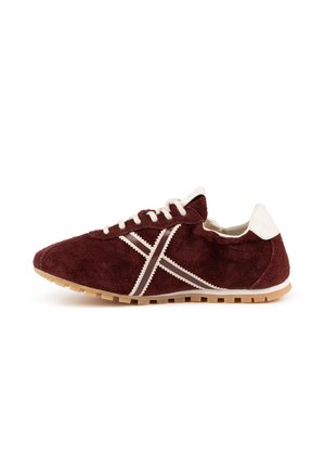 Zapatilla de ante color granate con cordones blancos, lengüeta blanca en el talón, rayas blancas cosidas en el lateral y suela de goma marrón clara.