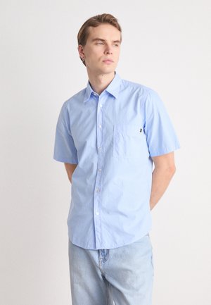 Camisa de manga corta azul claro de algodón, con frente de botones, un bolsillo de parche en el lado izquierdo del pecho y una textura sutil.