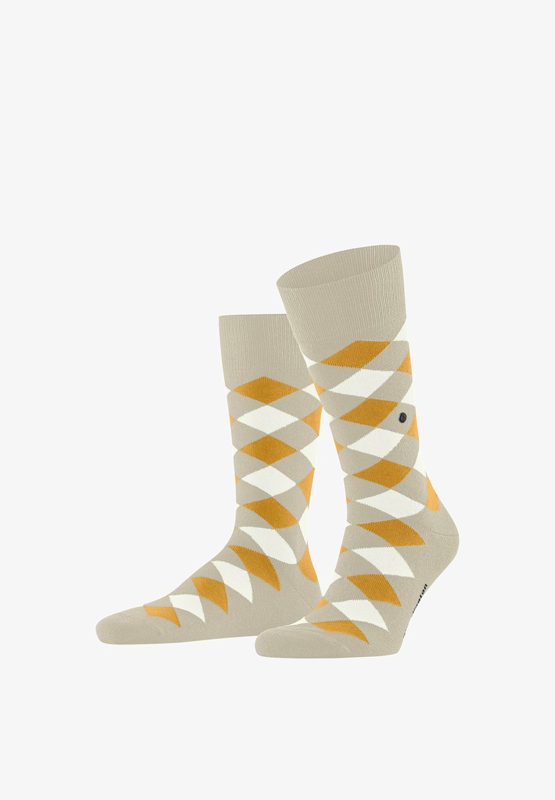 Chaussettes beiges avec motif argyle en forme de losanges orange, blanc et marron clair, une chaussette légèrement relevée et inclinée vers l'avant.