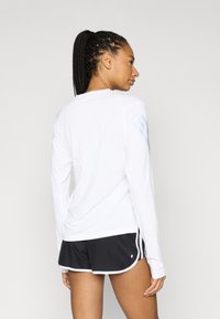 Top deportivo blanco de manga larga con rayas azules de acento en los hombros, combinado con pantalones cortos negros con ribete blanco. Tela suave, ajuste relajado.