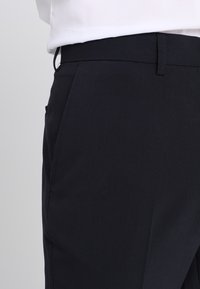 Marineblaue Hose mit tailliertem Schnitt, gefertigt aus glattem Stoff. Verfügt über einen flachen Bund, seitliche Taschen und dezente Nähte.