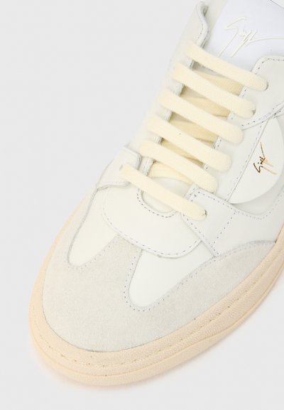 Valge nahast ja helehallist seemisnahast toss, millel on kreemjad paelad, sile pind, ümmargune ninaosa ja peen logo detail.