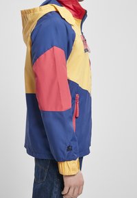 Kolorowa kurtka wiatrówka z panelami w kolorach niebieskim, żółtym i czerwonym, kieszenią na zamek oraz elastycznymi mankietami. Wykonana z lekkiego, wodoodpornego materiału.