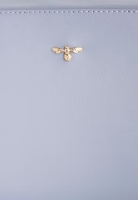 Articolo in pelle di un blu chiaro con una finitura testurizzata, caratterizzato da un emblematico ape dorata al centro. Dettagli di cucitura lungo i bordi.