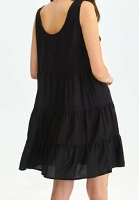 Schwarzes ärmelloses Kleid mit gestuftem Design, weichem Stoff und Rundrücken. Es zeichnet sich durch eine fließende Silhouette und einen rüschierten Saum aus.