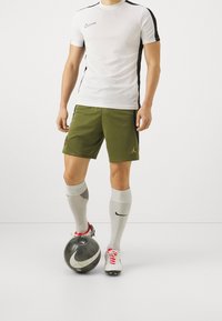 Nike vit t-shirt med kort ärm och svarta detaljer, olivgröna shorts med Jordan-logotyp, vita strumpor med ränder, röda och vita fotbollsskor, svart fotboll.