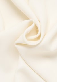Kremfarvet stof med en glat tekstur, der har bløde folder og draperinger. Overfladen er let skinnende, hvilket indikerer en syntetisk blanding.