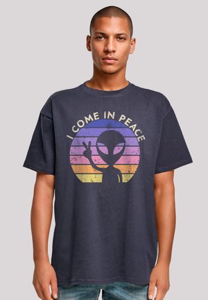 Navy blue cotton t-shirt featuring a graphic design of an alien with the text "I COME IN PEACE" and a sunburst in pink and yellow hues.
