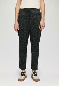Zwarte broek met een geometrisch patroon, elastische tailleband en drawstring. Gecombineerd met beige en zwarte casual sneakers.