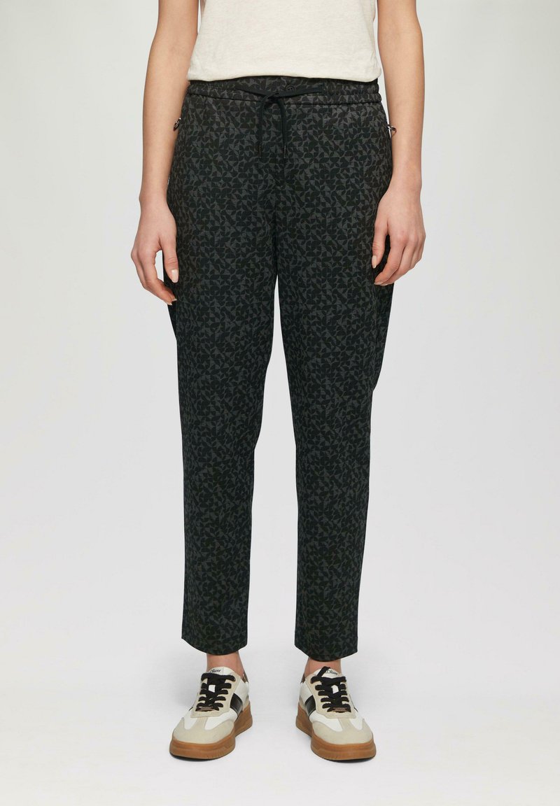 Zwarte broek met een geometrisch patroon, elastische tailleband en drawstring. Gecombineerd met beige en zwarte casual sneakers.