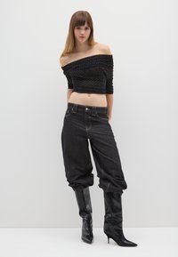 Top nero senza spalle con texture arricciata e pois bianchi, abbinato a pantaloni baggy in denim scuro e stivaletti neri con tacco a spillo al ginocchio.