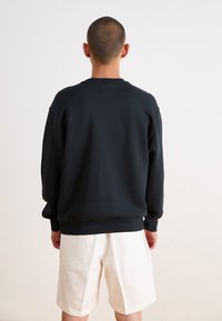 Dunkelgrauer Pullover mit langen Ärmeln, Rundhalsausschnitt und gerippten Bündchen, kombiniert mit hellen cremfarbenen Shorts. Glatte, lässige Stofftextur.
