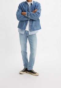 Denim takki rentoon istuvuuteen, sininen väri, etutaskut, kerrostettuna vaalean sinisen paidan päälle, yhdistettynä vaaleansinisiin farkkuihin ja mustiin lenkkareihin.