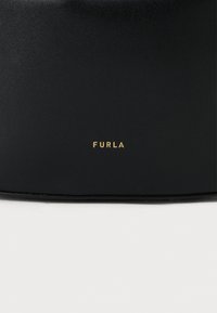 Bolsa de couro preta com acabamento texturizado e um logótipo "FURLA" dourado ao centro. Design compacto com uma forma suave e arredondada.