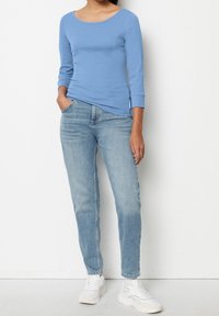 Lichtblauwe lange mouw shirt met een ronde hals, gecombineerd met lichtblauwe jeans en witte sneakers, met een casual, aansluitende pasvorm.