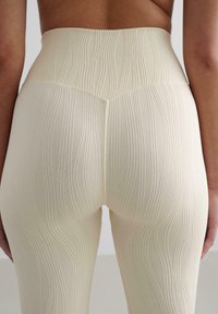 Leggings taille haute en crème clair avec un motif texturé en vagues, dotés d'un tissu lisse et d'une finition sans couture à la taille et aux jambes.