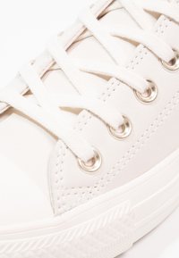 Baskets en toile blanche avec lacets plats, œillets métalliques et semelle en caoutchouc. Présente une semelle extérieure texturée et des coutures le long de la tige.