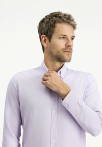 Camicia azzurra chiara con bottoni, realizzata in tessuto a trama, maniche lunghe e colletto a punta. Presenta piccoli bottoni bianchi lungo la parte anteriore.