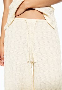 Pantalons de détente texturés couleur crème avec un motif ondulé, dotés d'une taille à cordon et d'une coupe ample pour le confort.