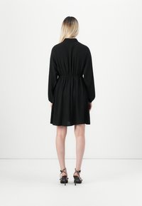 Black long-sleeve dress with a cinched waist and flared skirt. Made of lightweight fabric, features a collar and falls above the knee.