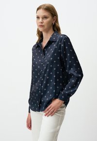 Navy blue zijden overhemd met knoopjes, versierd met kleine witte bloemenpatronen. Het heeft een klassieke kraag, lange mouwen en knoopmanchetten.