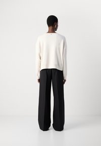 Crème sweatshirt met een ontspannen fit en een verlaagde schouderlijn, gecombineerd met hoge, zwarte, wijde broekspijpen. Soepele textuur, minimalistisch ontwerp.