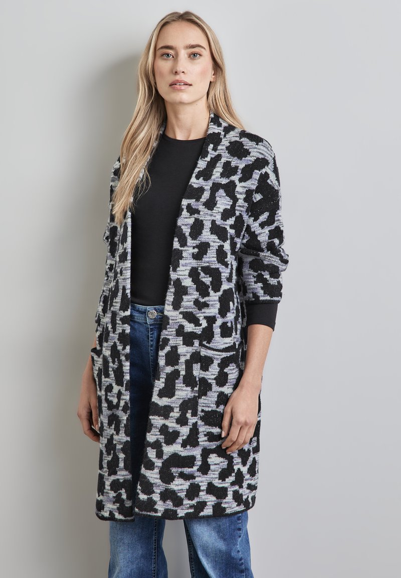 Knit cardigan in black and gray leopard pattern, with open front, long sleeves, and front pockets, paired with black top and blue jeans.