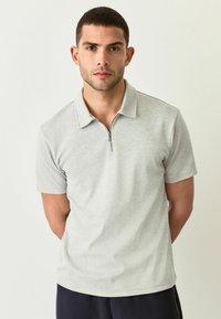 Polo de color gris claro con un patrón de espiga, mangas cortas, cuello con cremallera y una suave textura de tela.