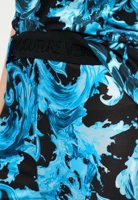 Κοντινή λήψη μαύρου υφάσματος με ζωντανό μπλε στροβιλιστό λουλουδάτο σχέδιο και μαύρη ζώνη μέσης με ανάγλυφο κείμενο.