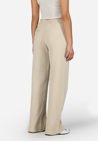 Beige széles lábú nadrág texturált, gofris mintázattal; elasztikus derék; oldalzsebek; szegélye kissé a lábbeli felett végződik.