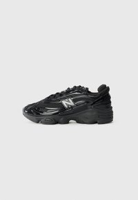 Black running shoe with glossy leather and mesh upper, prominent New Balance logo, thick rubber sole, and textured detailing.