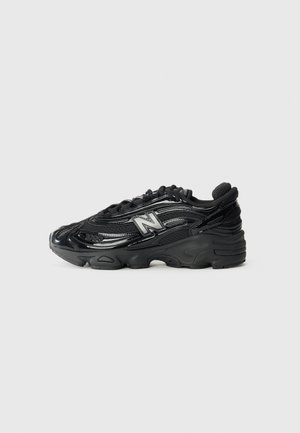 Zapatilla de running negra con parte superior de cuero brillante y malla, logo de New Balance prominente, suela de goma gruesa y detalles texturizados.