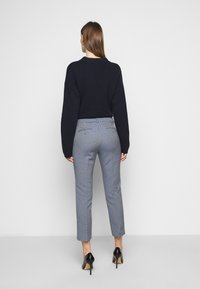 Maglione a maglia blu navy e pantaloni blu a motivo con vestibilità slim, abbinati a scarpe nere con tacco alto. Vista da dietro.