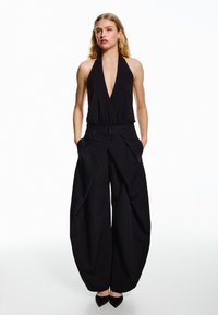 Czarny kombinezon z głębokim dekoltem w serek, elastyczną talią i szerokimi nogawkami. Gładka tkanina z kieszeniami i zapięciem na dwa guziki. Prosty wzór.
