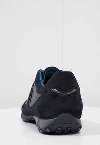 Ciemnoniebieskie zamszowe buty o teksturowanym wykończeniu, z czarną skórzaną wstawką i fioletowymi akcentami na gumowej podeszwie. Wyświetlony widok z tyłu.