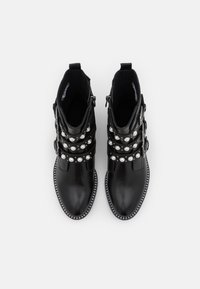 Botines de cuero negro con múltiples correas y acentos de perlas redondas, punta afilada y una suela decorativa con tachuelas. Tacón plano.
