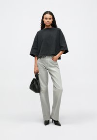 Fekete, oversized, rövid fazonú póló, szürke egyenes lábú farmer, fekete magassarkú cipő és egy kisméretű fekete kézi táska. Sima textúrák és minimalista design.