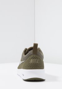 Nike-sneaker med en grön mesh-överdel, vit mellansula och bakre dragflik; har synliga perforeringar och präglar logotypen på hälen.