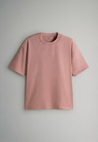 Camiseta rosa de manga corta con cuello redondo, confeccionada en tela suave, que presenta un ajuste holgado y un diseño simple y limpio.
