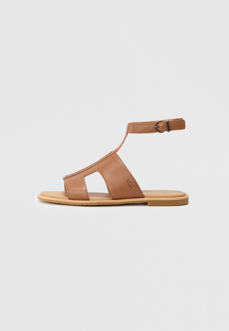 Bruine lederen sandaal met een platte zool, open teenontwerp en enkelriem. Beschikt over uitgesneden zijkanten en een eenvoudige gesp voor aanpassingsmogelijkheden.