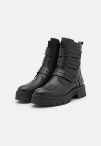 Bottines noires en cuir lisse, avec cinq sangles horizontales, une semelle épaisse et un design de bout rond.