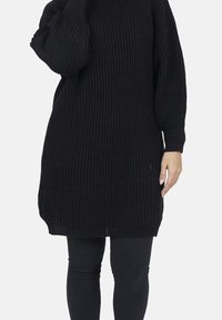 Sort strikket tunikakjole med ribbet tekstur, lange ærmer og en let oversized pasform. Fremhævet af løse manchetter og en rundet kant.