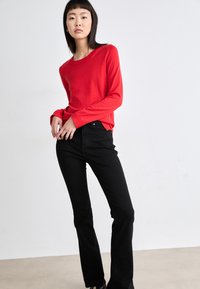Suéter rojo de manga larga con cuello redondo, combinado con jeans negros ajustados. Diseño sencillo, textura suave y colores sólidos.