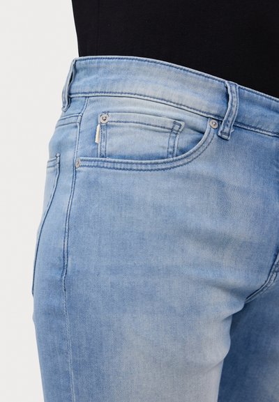 Jeans en denim bleu clair avec une apparence délavée, présentant une taille haute, deux poches avant et des détails en métal sur les boutons.